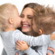 A mother smiling with two children kissing her cheeks on both sides