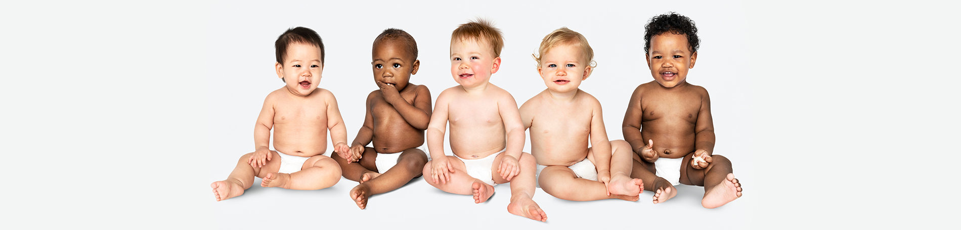 Sitting in a row there are five happy babies in nappies all from all different ethnicities