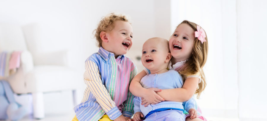 Two children laughing and holding their baby brother