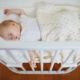 Baby fast asleep on her back in the cot veiwed from above