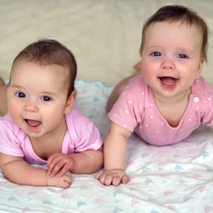 Very happy twin baby girls on their tummies looking up and smiling
