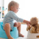 A blond toddler on a potty holding his teddy sitting on another potty