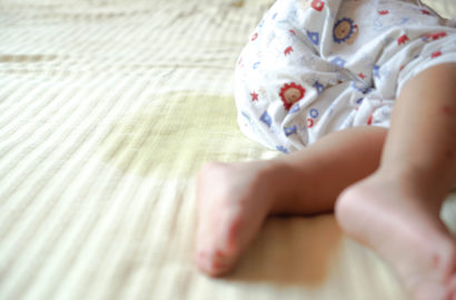 child in pyjamas with a wet patch on the sheet where the child has wet the bed