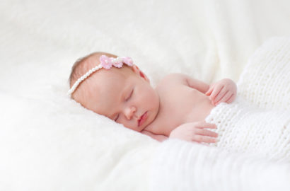 1 month old baby girl with a pink headband sleeping peacefully on her back with a blanket laid over her waist