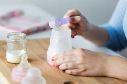 A mothers hands using a measuring spoon to put formula power into the baby bottle